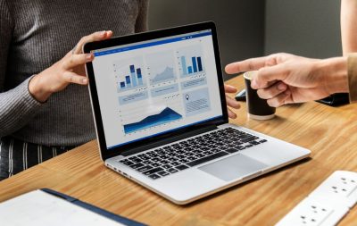 A woman shows a laptop displaying various marketing metrics to her colleague.