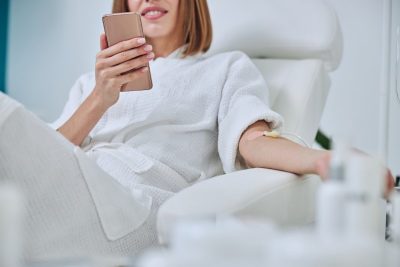 A woman in a medspa getting an injectable treatment while holding her phone.